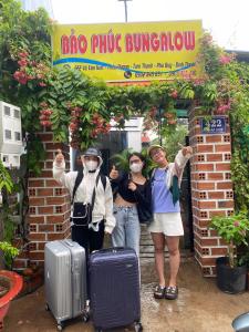 trois personnes portant des masques debout sous un panneau avec des bagages dans l'établissement Bảo Phúc Bungalow- Đảo Phú Quý, à Cu Lao Thu