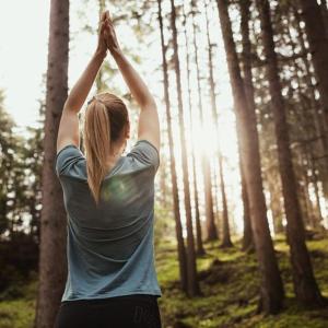 Una donna in piedi in una foresta con le mani in alto di Hotel Corno Bianco a Nova Ponente