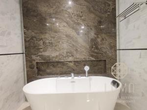 a white bath tub in a bathroom with a stone wall at The Platinum 2 Kuala Lumpur by LUMA in Kuala Lumpur