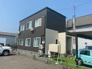 una casa negra con un coche aparcado delante de ella en 夢富良野 en Furano