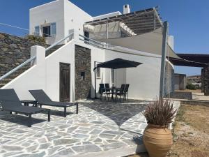 a white house with a patio with chairs and an umbrella at ΑΤΕΛΙΟΥ ΣΤΟΥΝΤΙΟ in Vari