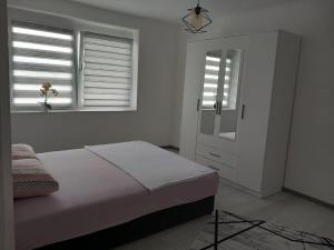 a white bedroom with a bed and two windows at Apartman Nea in Sanski most