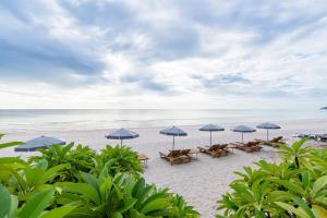 a beach with tables and umbrellas and the ocean at Veranda Lodge in Hua Hin