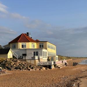 a yellow house on the beach next to the water at Havsbadens B&B in Ängelholm