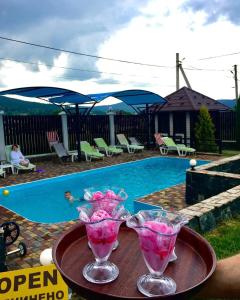 dos vasos de martini sentados en una mesa junto a una piscina en Villa Grand en Skhidnitsa