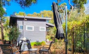 un patio con sillas, sombrilla y cobertizo en Aurora Cottage en Hepburn Springs