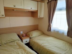 Duas camas num pequeno quarto com uma janela em 2 Bedroom Static Caravan C3 on quiet park near Talacre and Prestatyn em Prestatyn