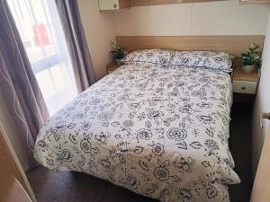 uma cama com um edredão azul e branco e uma janela em 2 Bedroom Static Caravan C3 on quiet park near Talacre and Prestatyn em Prestatyn