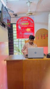 a man sitting at a counter with a laptop computer at Hotel Rose Haven Residential in Dhaka