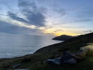 a sunset over the ocean with rocks on a hill at Carraig Inn in Derreen