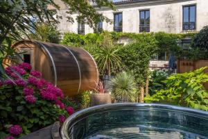 a garden with a barrel and flowers in front of a building at Escale Rochelaise, gîte urbain avec SPA bain nordique et sauna tonneau in La Rochelle