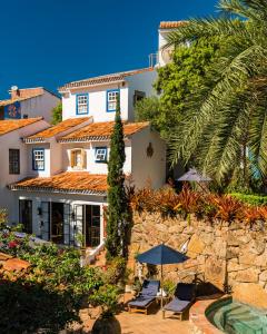 a house with a stone wall and two chairs and an umbrella at Vila da Santa Hotel Boutique & Spa in Búzios