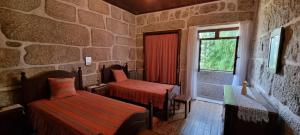 a room with two beds and a window in a stone wall at Moradia no Gerês - O Africanista in Soengas