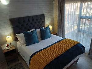 a bedroom with a large bed with blue pillows and a window at Cinnamon & Sage Country Cabins in Dullstroom