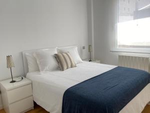 a white bed with a blue blanket and a window at Apartamento Lea in Bilbao