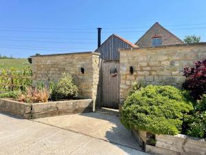 a stone building with a wooden gate and some bushes at The Cow Shed - Rural Barn Conversion in Little Bytham
