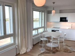 uma cozinha com uma mesa branca, cadeiras e janelas em Goldfinger saunallinen kaksio merinäköalalla 11 krs em Helsinque