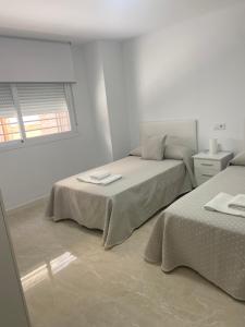 a white bedroom with two beds and a window at VIVIENDA RURAL EL PROGRESO in Carchelejo