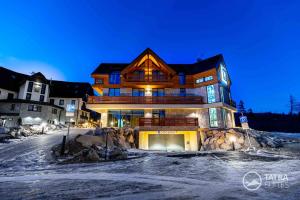 un gran edificio de madera en la nieve por la noche en TATRA SUITES Vila HIMALAYA, en Tatranská Lomnica