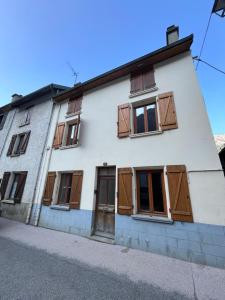 ein weißes Haus mit Holztüren und Fenstern in der Unterkunft Townhouse The Granary Bourg d’Oisans in Le Bourg-dʼOisans