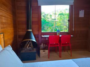 um quarto com uma mesa, 2 cadeiras vermelhas e uma lareira em Refúgio Allamanda Flats em Visconde de Mauá
