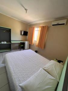 a bedroom with a white bed and a desk at Hotel Peritoró in Peritoró