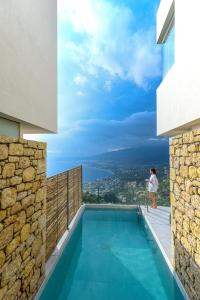 a woman standing on the balcony of a house with a swimming pool at Lithos Retreat 1 in Káto Sélitsa