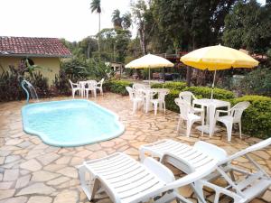 - une piscine avec des chaises, des tables et un parasol dans l'établissement Pousada Quintão, à Santana do Riacho