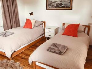 1 dormitorio con 2 camas con almohadas de color naranja en The Anchorage- A waterfront 70’s retreat, en Dora Creek