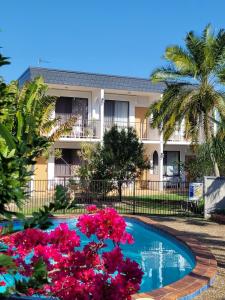 a pool in front of a building with pink flowers at Tower Court Motel - adults only haven in Hervey Bay