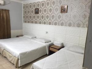 2 bedden in een hotelkamer met witte lakens bij Lily Budget Hotel in Jertih