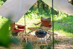 a picnic table with a grill and chairs under a tent at Morino Chalets in Hakuba