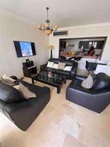 Luxueux appartement à la Marina d’agadir في أغادير: غرفة معيشة مع أثاث من الجلد الأسود وتلفزيون بشاشة مسطحة