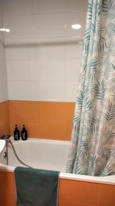 a bath tub with a shower curtain and a green chair at Apartamento Mirador de Padin in Ribeira