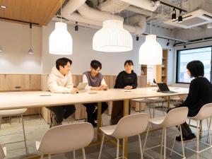 a group of people sitting around a table in a room at Hotel Plus Hostel SAPPORO in Sapporo