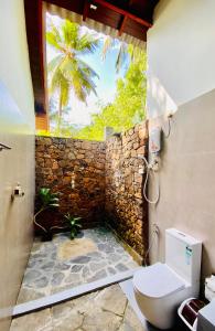 a bathroom with a toilet and a stone wall at Mango Tree House in Udawalawe