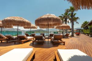 eine Terrasse mit Liegestühlen und Sonnenschirmen am Strand in der Unterkunft Ala Suites and Villas Yalıkavak in Yalıkavak