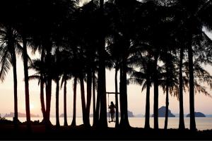 a couple standing under palm trees on the beach at Phulay Bay, A Ritz-Carlton Reserve in Tab Kaek Beach