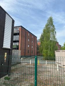 uma cerca em frente a dois edifícios e a uma árvore em Priestley Court em Warrington