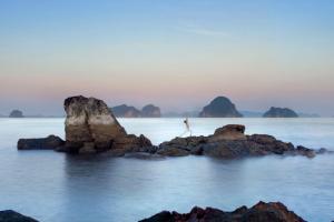 a person standing on rocks in the water with mountains in the background at Phulay Bay, A Ritz-Carlton Reserve in Tab Kaek Beach
