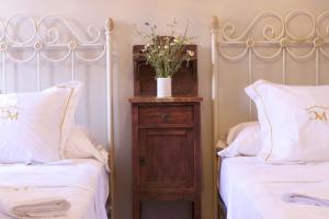 2 camas con sábanas blancas y mesita de noche de madera entre ellas en Casa Rural Melitón, en Povedilla