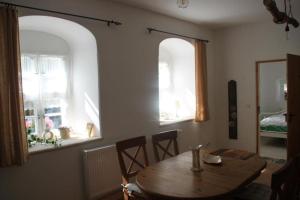 a dining room with a wooden table and two windows at Hofmühle Pfaffroda-Ferienwohnung Am Mühlbach in Olbernhau
