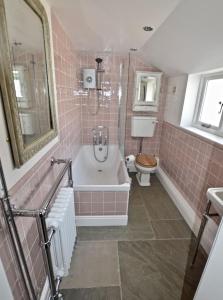 a pink tiled bathroom with a tub and a toilet at Skylarks - Cley next the Sea - Crabpot Cottages. in Cley next the Sea