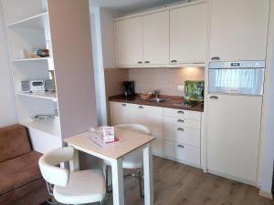 ヴェスターラントにあるSylter-Besserburg-Appartement-1の小さなキッチン(白いキャビネット、テーブル、椅子付)