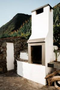 een wit gebouw met een open haard naast een stenen muur bij Abrigo dos Bodes - Goat's Shelter in Calheta