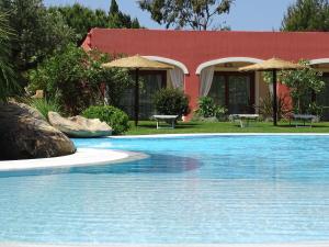 a swimming pool in front of a red building at Hotel Mariposas in Villasimius