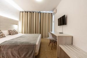 Habitación de hotel con cama y escritorio con TV. en Hotel Ecoavenida en Benicàssim