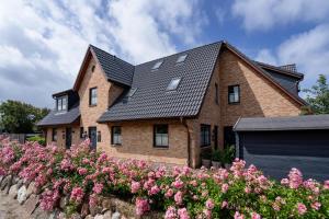 uma casa de tijolos com um telhado preto e flores cor-de-rosa em Zweite Heimat em Westerland