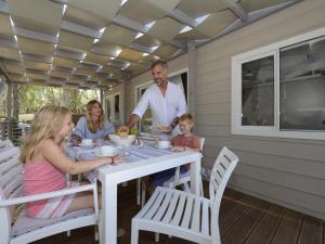 una familia sentada en una mesa comiendo comida en un porche en Detached chalet with AC, in a natural park on the coast, en Baia Domizia