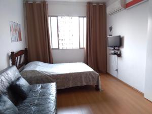 a bedroom with a bed and a couch and a window at Lindo Studio na Praia do Gonzaguinha II in São Vicente
